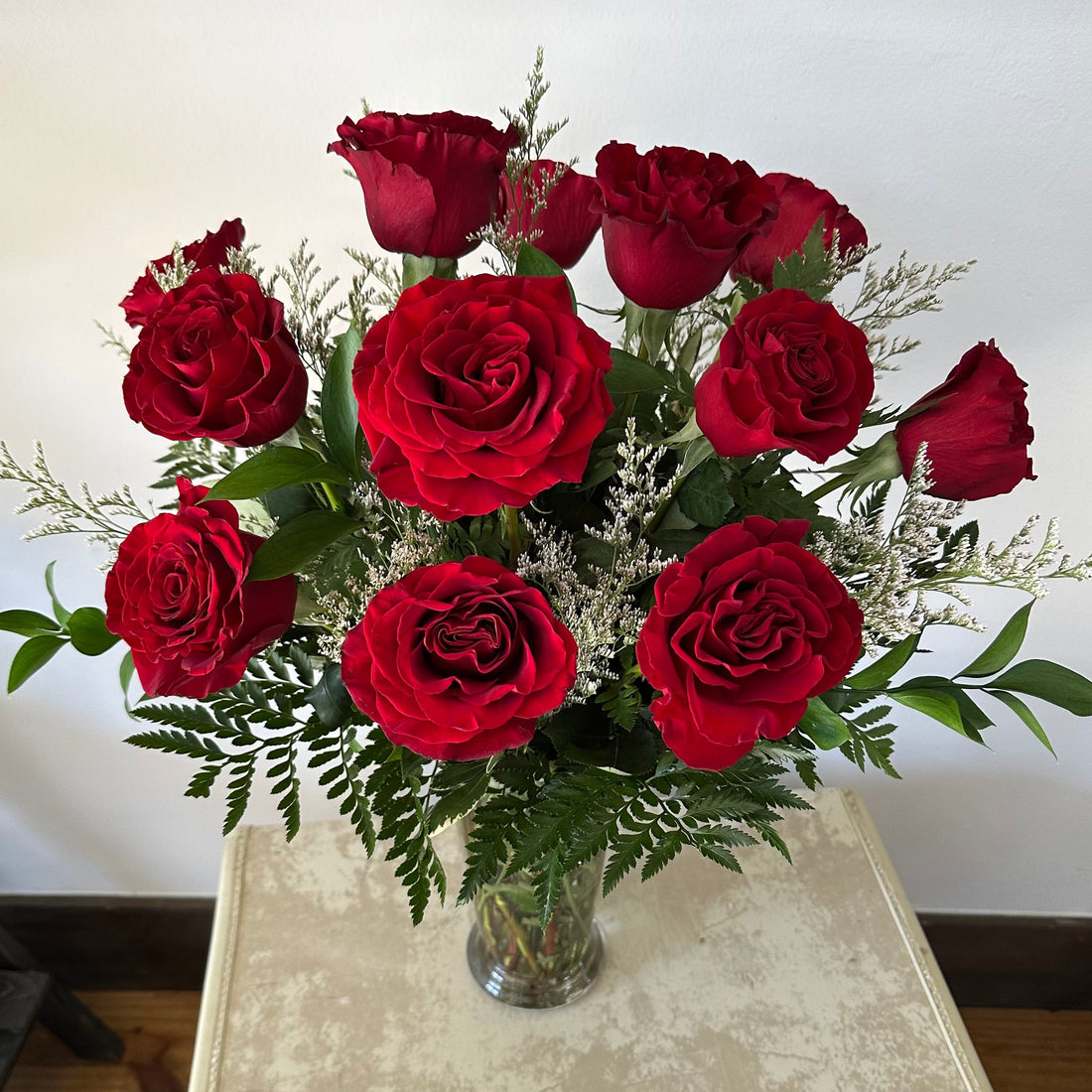 Timeless red roses arranged in a glass vase with assorted greenery and white filler